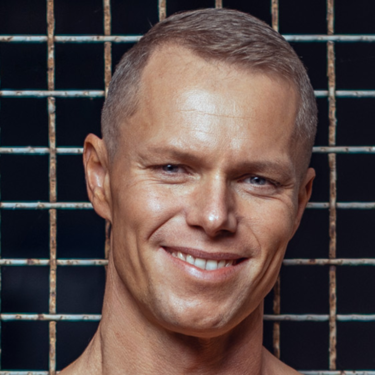 Tim Lühmann von TWL Fitness Lächelnder Mann mit kurzem Haar vor einem Gitterhintergrund.